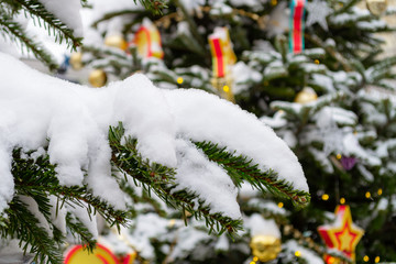 Christmas decorations. Branches of real spruce covered with snow. Close-up. Another fir tree decorated with Christmas toys in the background. Bokeh. Xmas