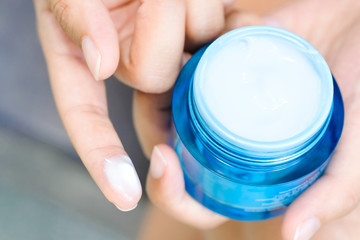 Hand of woman holding moisturizer cream and serum. She applying a facial cream , essential , oil , lotion and body cream for skin care, close up view and blur background. Beauty and Healthy Concept.