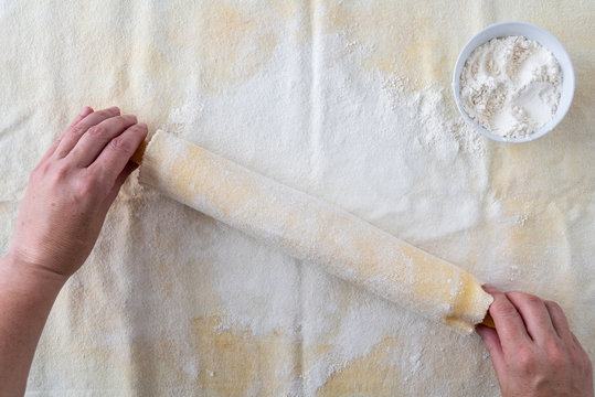 Woman’s hands on wood rolling pin, cloth covered, flour covered pastry cloth, small bowl of flour