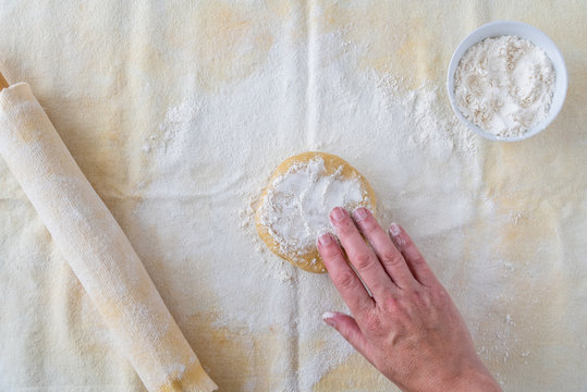 Woman’s hand dropping flour on ball of cookie dough, pastry cloth, wood rolling pin with cloth cover, small bowl of flour