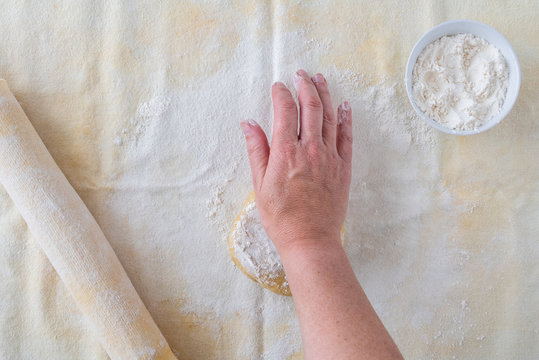 Woman’s Hand Dropping Flour On Ball Of Cookie Dough, Pastry Cloth, Wood Rolling Pin With Cloth Cover, Small Bowl Of Flour