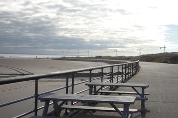 Fototapeta na wymiar Sky, sand, sea, and boardwalk with tables and railings 