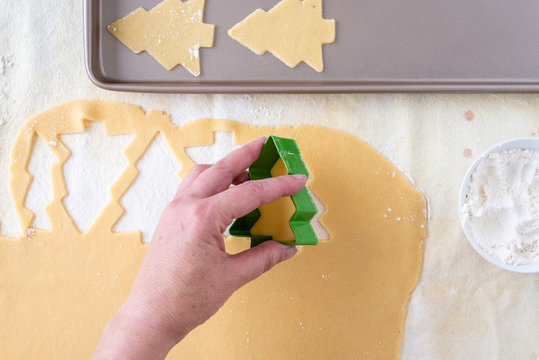 Woman’s hands cutting out Christmas tree sugar cookies, pastry cloth, cookie sheet