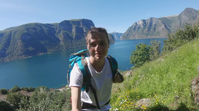Young woman backpacker taking a selfie on the background of a Norwegian fjord on a sunny day. Adventure mood.