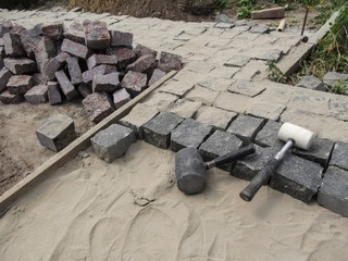 In the process of laying black and red granite pavers. The site where the work on laying paving slabs, a pile of stones and tools for laying tiles