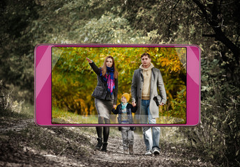 Young parents with little son walking in forest, saturated image in smartphone s camera