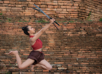 A beautiful girl in a red dress holding a double sword at the old temple.