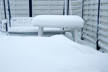 a thick white blanket of snow covers garden furniture standing on a terrace