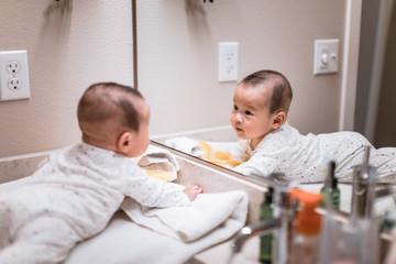 Adorable 5 month old asian baby boy in looking into bathroom mirror