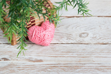Greeting card for Valentine's Day. Pink textured heart on a white wooden background. Green twigs around the edges for decoration.