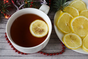 A wooden background with Christmas decorations. A cup of hot tea with lemon.