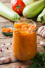 Homemade caviar from zucchini tomatoes and onions in a glass jar on a wooden background. Homemade production canning, canned stewed vegetable.