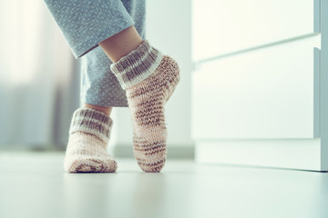 Woman in pajamas and cozy soft warm knitted winter socks at home
