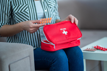 A woman holds a medical first aid kit with medicine at home