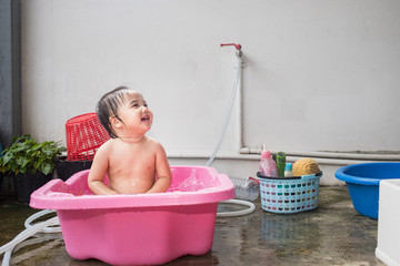 Baby kid taking a bath in pink bathtub and making water splash