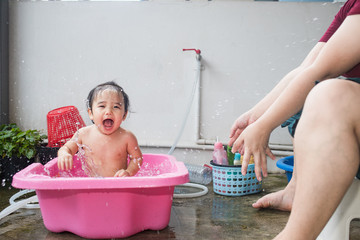 Baby kid taking a bath in pink bathtub and making water splash