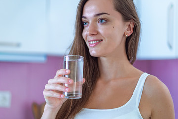 Happy attractive healthy drinking woman holding glass of clean purified water in hands in the morning in the kitchen at home. Healthy lifestyle