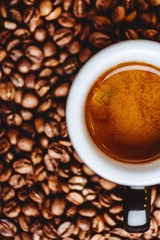 Roasted coffee beans with cup of espresso on dark background