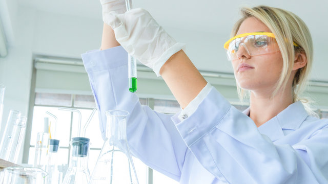 close up face of female scientist holding a tube and beaker with liquid substance. woman research is working in the Laboratory.