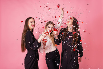 Three women celebrate the New Year party having fun laughing under the flying confetti and drinking...