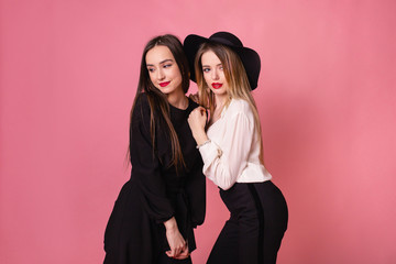 Two beautiful girls celebrate corporate party. Girls smiling and posing on pink background, bright makeup, red lips 