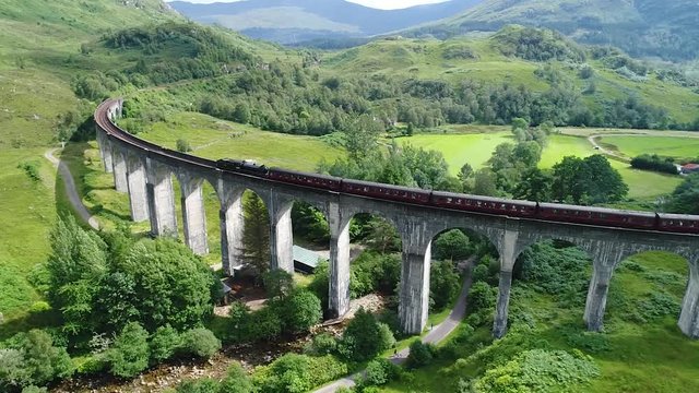 the ancient steam train also known as jacobite, is passing on the old viaduct built in 1900 in the wonderful glenfinnan valley in scotland.