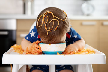 Funny baby eating pasta straight from bowl