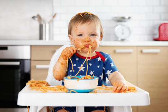 Funny baby eating spaghetti with his hands