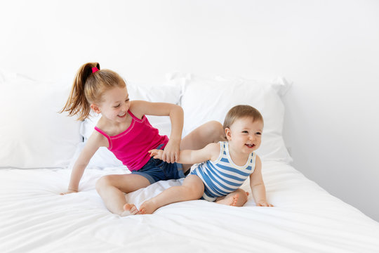 Baby boy and big sister playing on white bed