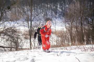 Fototapeta na wymiar A boy in a ski suit on a snow mountain with a sled. The child is riding a sledge scooter . Active games on the street. Healthy lifestyle