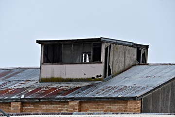 Derelict building dormer with broken louvre windows, clad with cement sheeting,atop the rusted iron roof an old abandoned factory made of bricks in Gippsland, Victoria, Australia,..