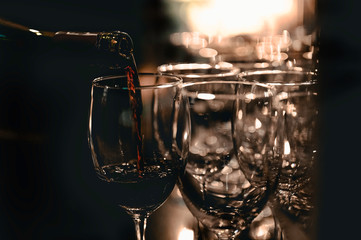 The bartender is pouring red wine in glasses and many empty glasses on the bar counter. Blurred background