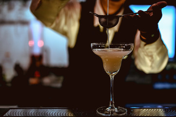 The young bartender is making a cocktail and decorating it in a martini cocktail glass for beautiful at a nightclub bar.