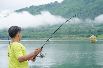 Fisherman spinning reel on the lake misty morning.