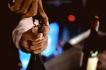 The bartender opens a bottle of red wine using a wine opener. To pour a lot of empty glasses at the...