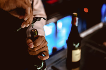 The bartender opens a bottle of red wine using a wine opener. To pour a lot of empty glasses at the...