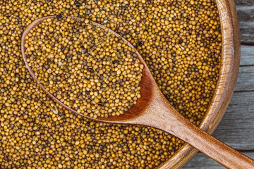Mustard seeds in wooden plate with spoon on table. Cooking porridge, healthy food