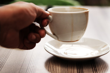 Man's hand holds a cup of coffee on wooden table.