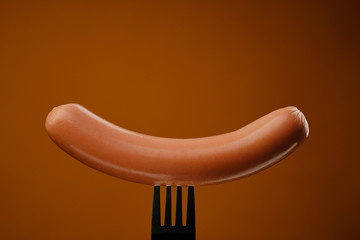 sausage on a fork isolated. brown background
