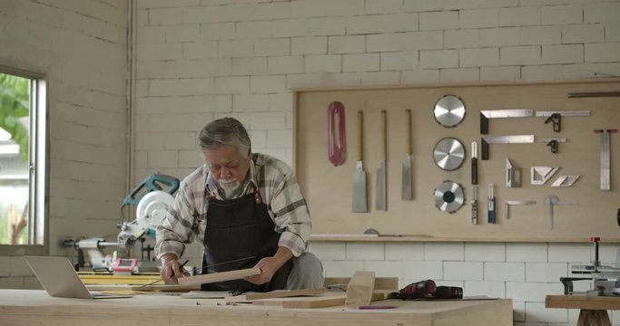Asian senior carpenter works in carpentry workshop during the day.