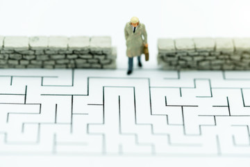 Miniature people: Businessman walking to wall in maze. Concepts of finding a solution, problem solving and challenge.