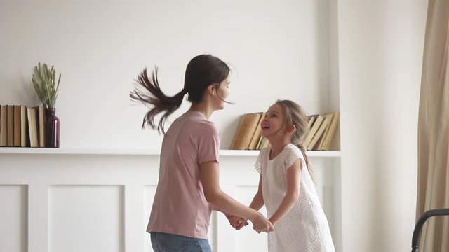 Active mother holding hands with daughter jumping on bed
