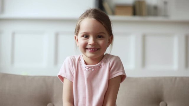 Little girl sitting on couch wave hand looking at camera