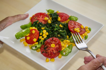 woman holding plate of spinach, tomato, corn and pepper salad, diet and food concept