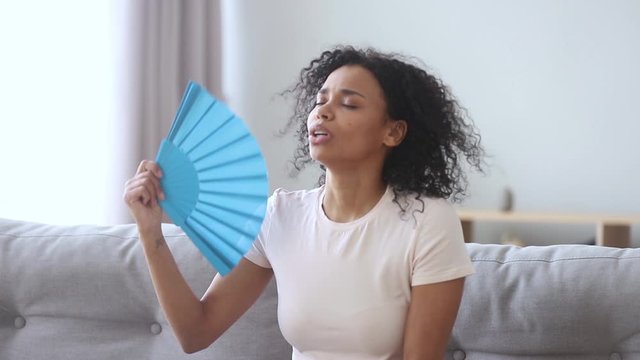 African woman feels hot waving fan annoyed with high temperature