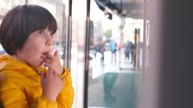 Child sucks fingers while standing at a shop window in a city.