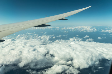 Fototapeta premium Plane’s wing above the clouds view from a plane's window with the blue sky.