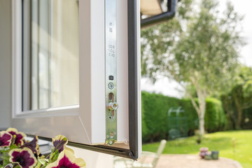 Close-up of a brand new installed double glazed window showing the multiple security locks on the frame. Part of a large garden and patio is seen on the right.