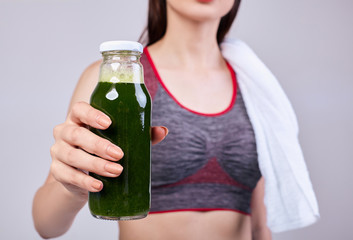 A girl of beautiful appearance athletic build holds a bottle with a healthy drink in her hand. Dark green cucumber cocktail, avocado, kiwi, vitamin drink. Healthy lifestyle. Sports, gym, well-being.