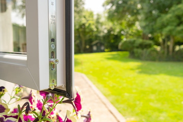 Close-up of a brand new installed double glazed window showing the multiple security locks on the frame. Part of a large garden and patio is seen on the right.